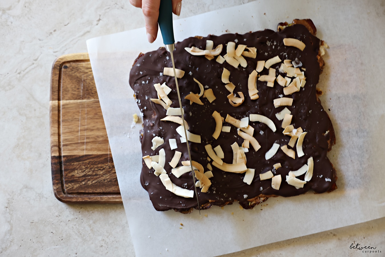 Slicing date bark on a piece of parchment on a wooden cutting board.