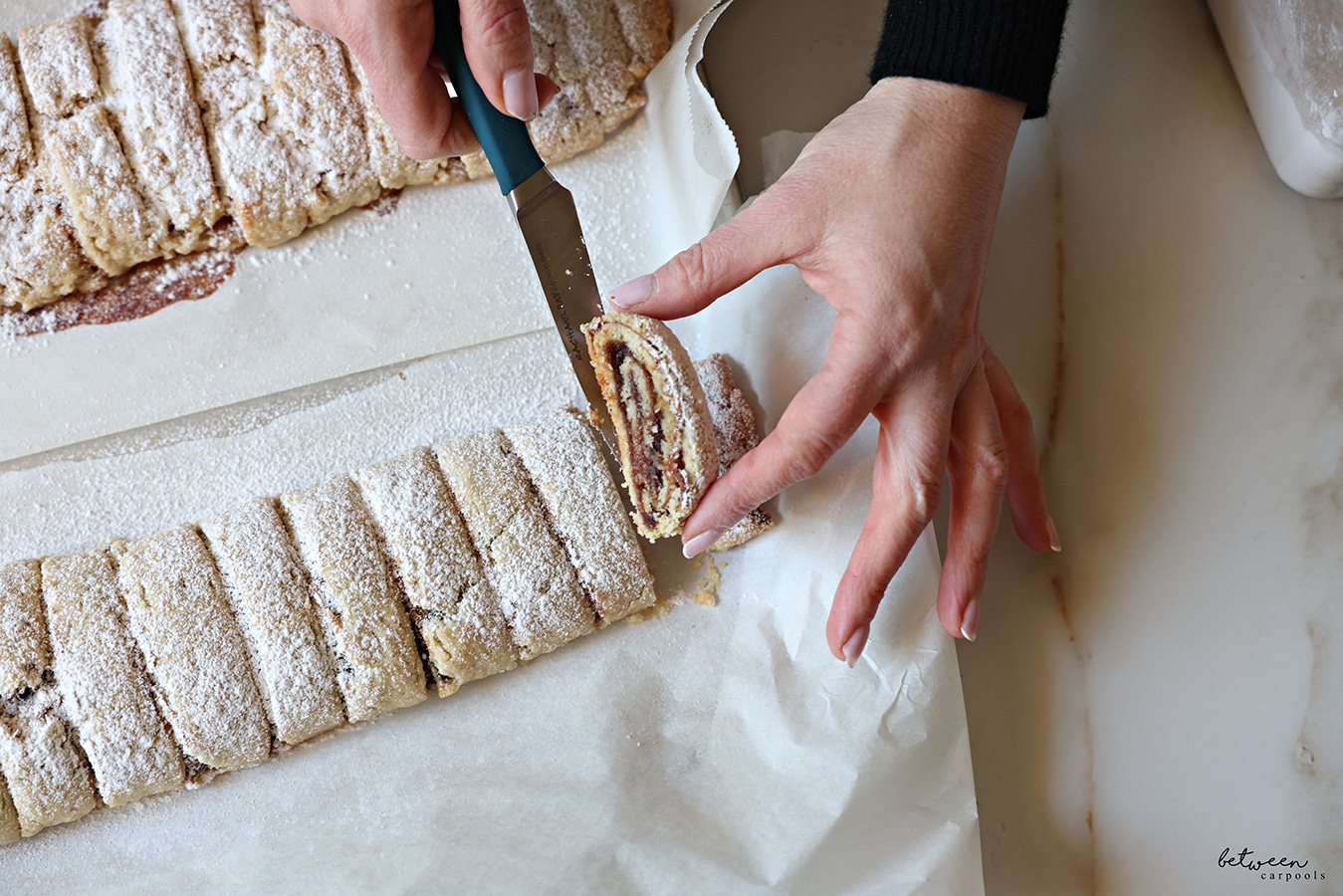 Lifting one date spread cookie. 2 rolls of baked date spread cookies with confectioners' sugar.