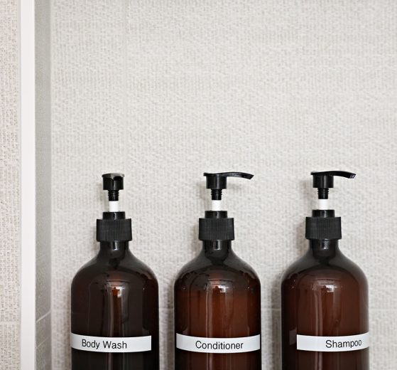 Three Amber Pump Bottles labeled Body Wash, Conditioner, and Shampoo, on a shower niche shelf.