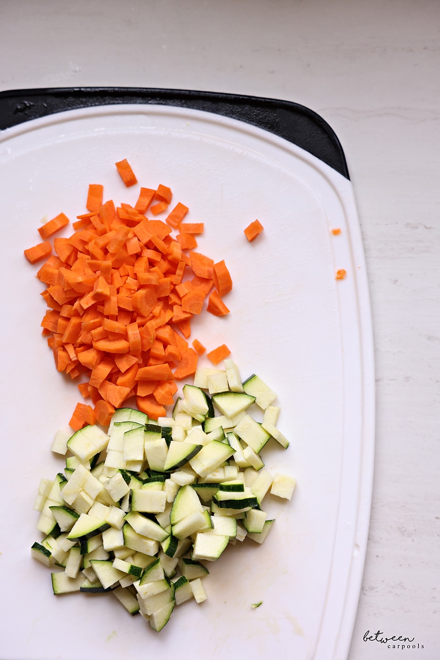 Diced zucchini and carrots on a plastic cutting board.