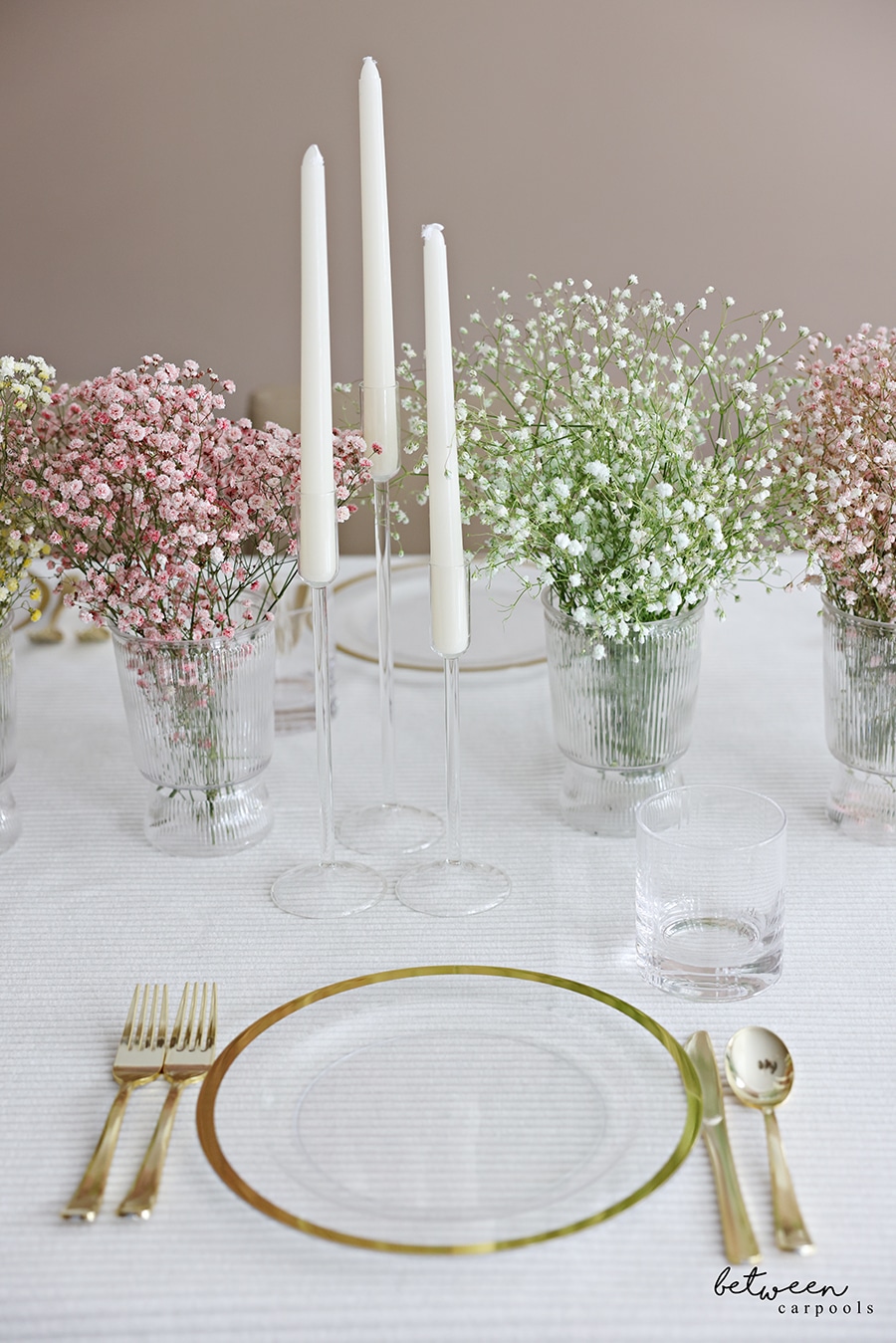 Closeup of table set with a cloth, plates, flatware, candles and colored baby's breath in vases.