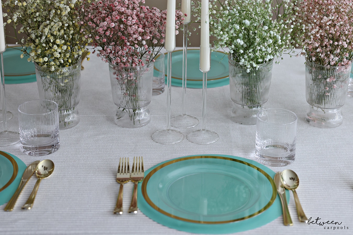 Table set with a cloth, paper placemats, plates, flatware, candles and colored baby's breath in vases.