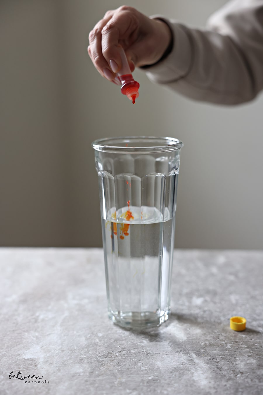 Adding drops of yellow food coloring into a glass tumbler of water.