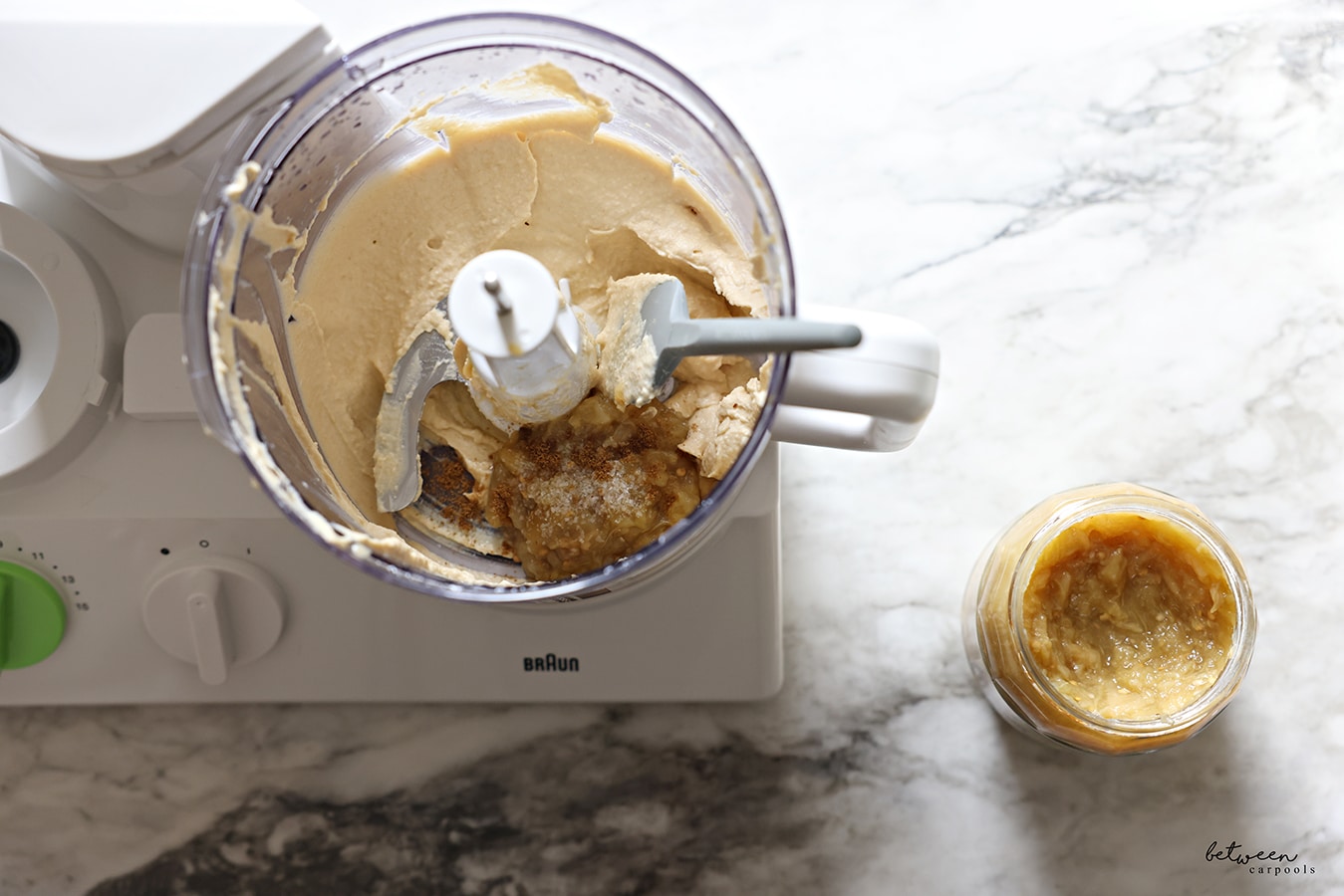 Half a cup of Galil fire roasted grilled eggplant in the bowl of a braun food processor - with the s blade and a spatula - with homemade chummus. Galil jar nearby.