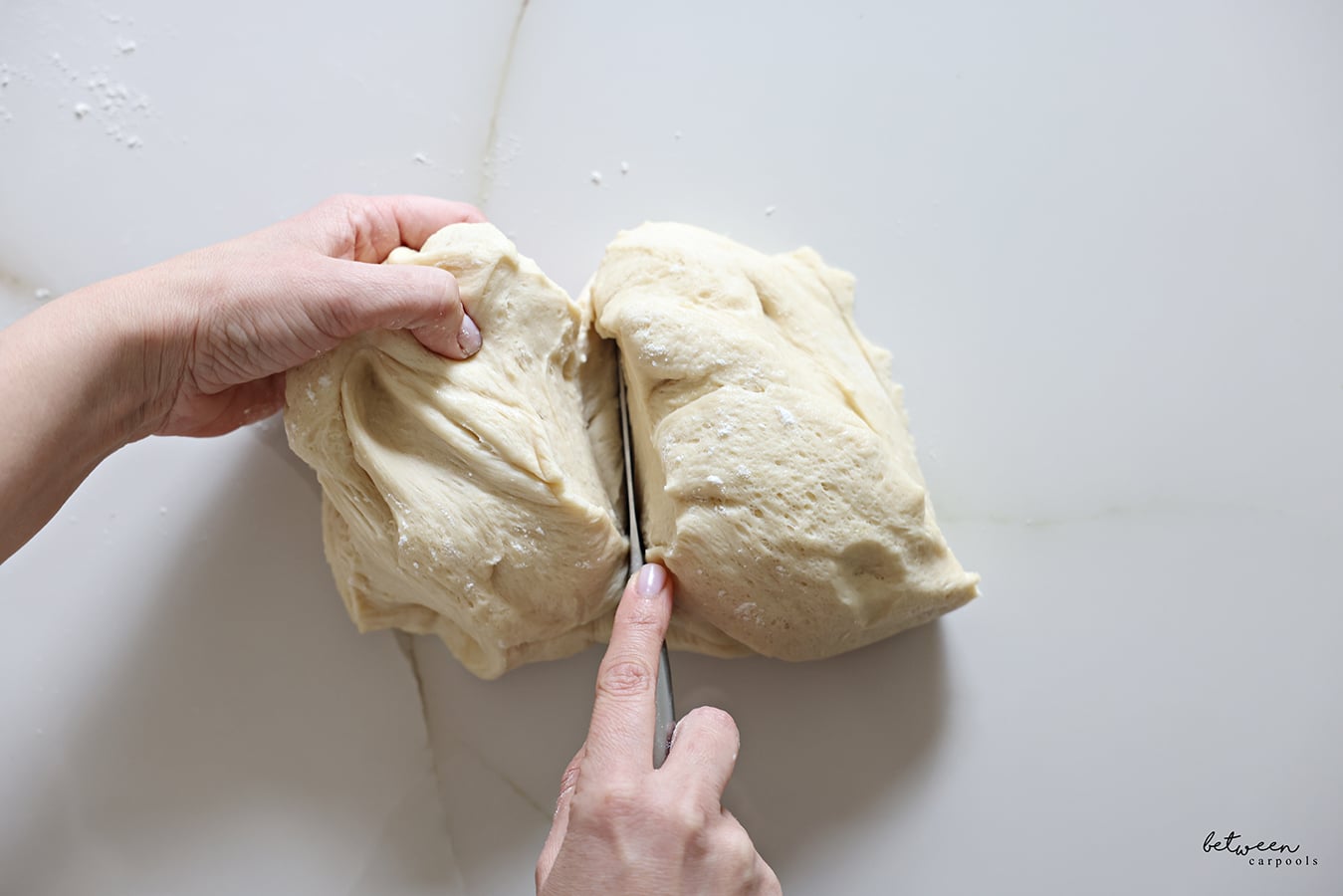 Cutting a piece of challah dough in half.