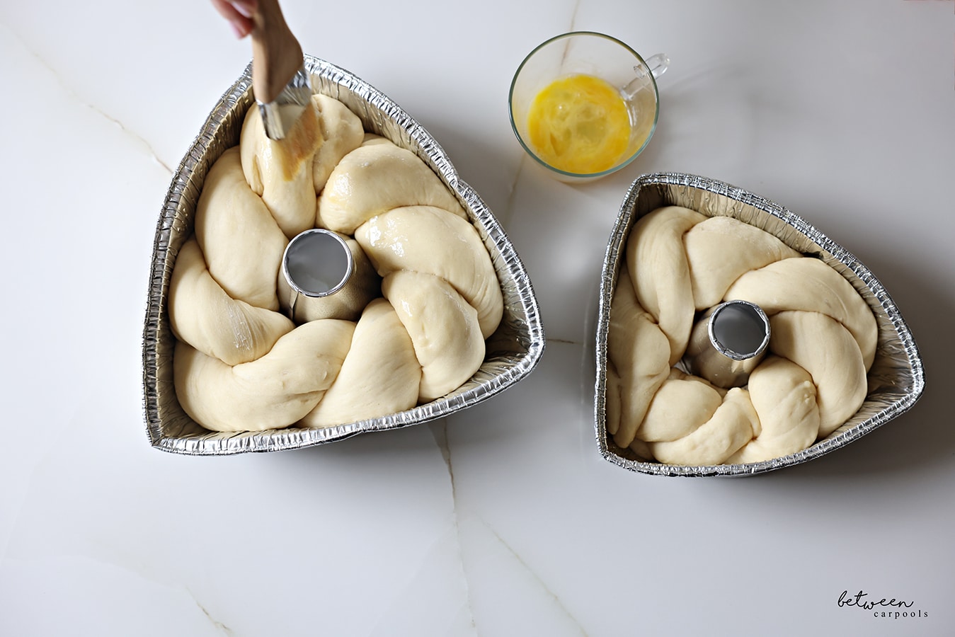Brushing the challah twists - made by twisting two longs strands of challah dough - wrapped around the tube of an 8" and 10" aluminum foil tube pan with its sides bent in to resemble triangles - with egg.