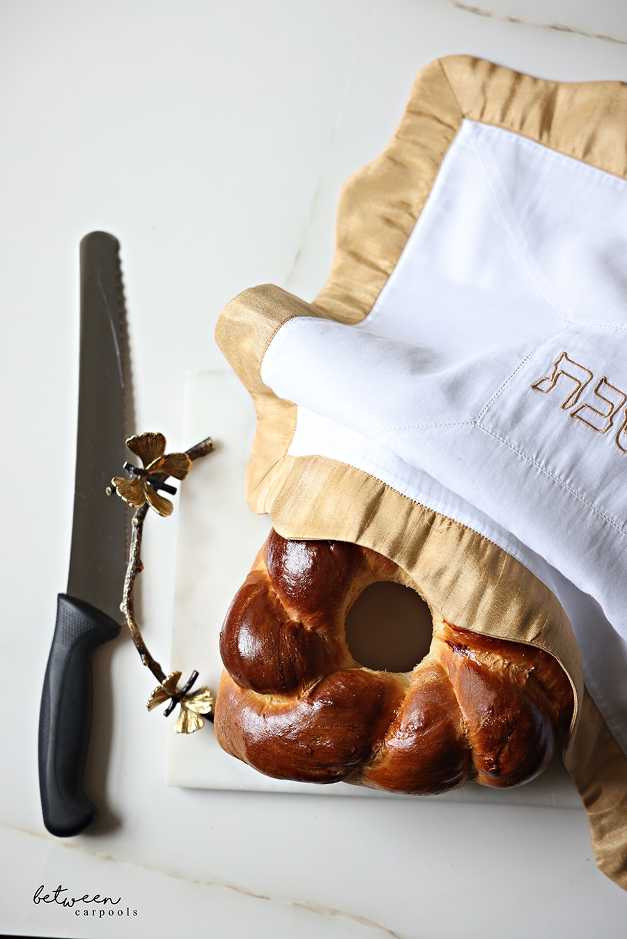 A Hamantaschen Shaped Challah on a challah board with a challah cover, and a bread knife nearby.