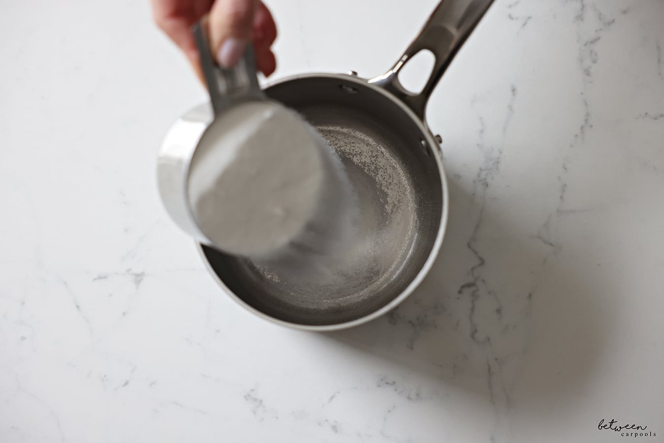 Pouring 1 cup sugar into a saucepan.