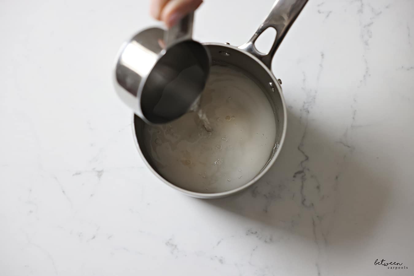 Pouring 1 cup water into a saucepan with 1 cup sugar.