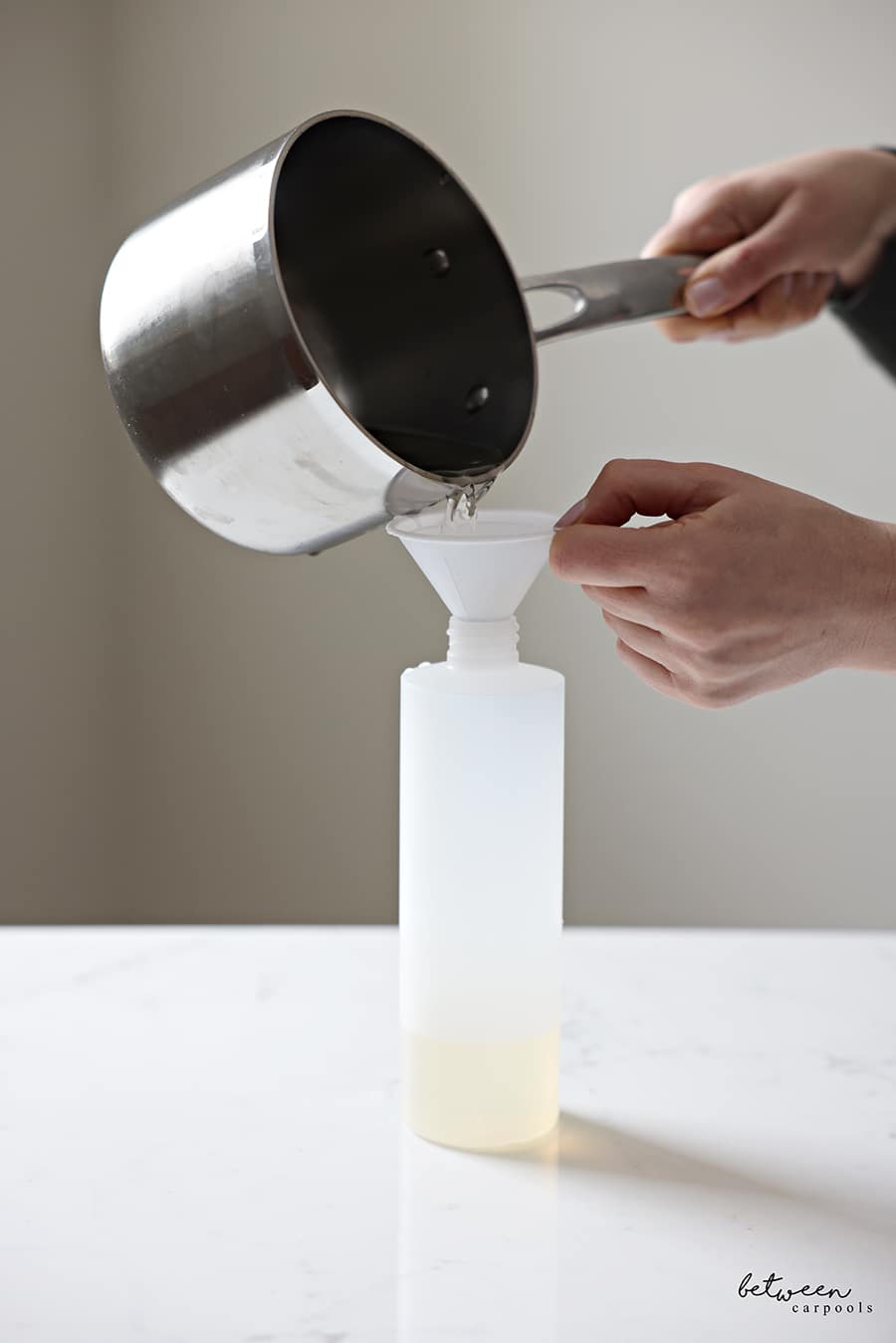 Pouring simple syrup (from a saucepan) through a funnel into a squeeze bottle.
