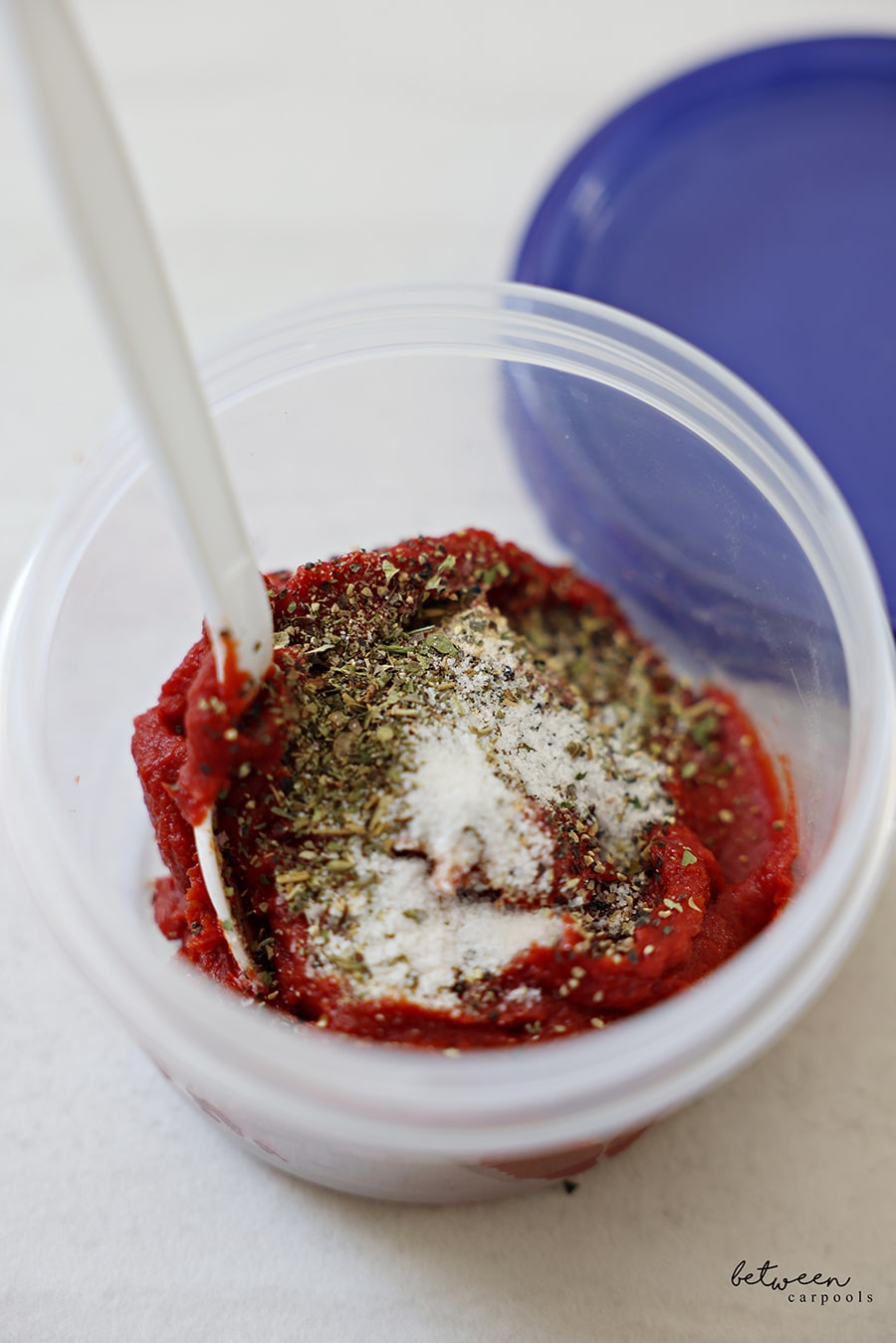 A 16 oz twist top storage container with tomato paste, seasoning, and a plastic spoon.