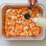 Filling a tbsp with oil over a 9x13 pan with sweet potato chunks and whole garlic cloves.
