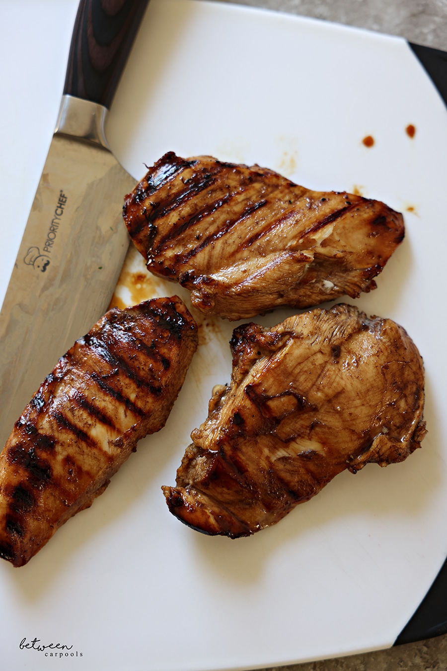 Chicken breast, marinated and grilled, on a plastic cutting board.