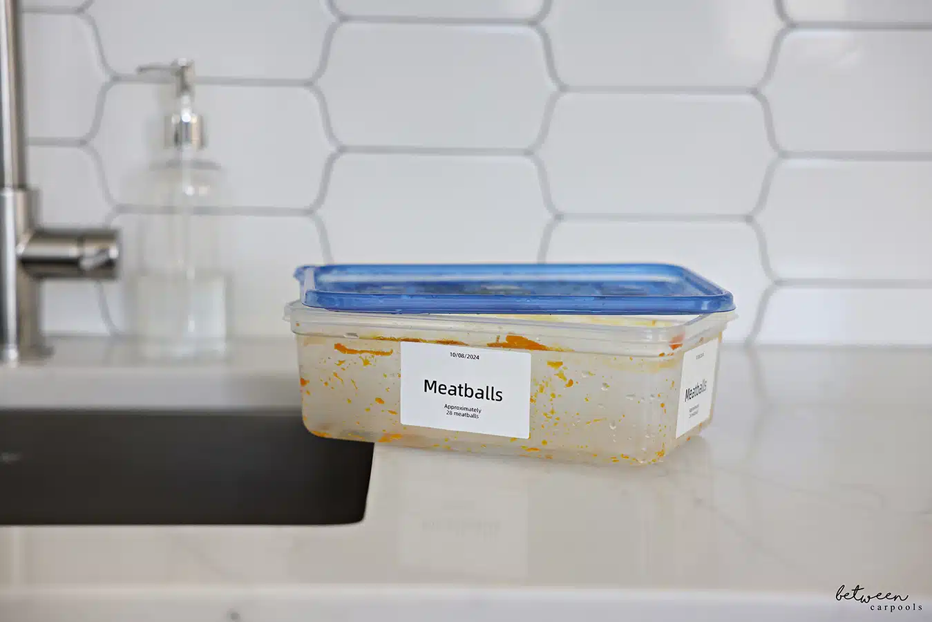 Dirty container labeled Meatballs near a kitchen sink.