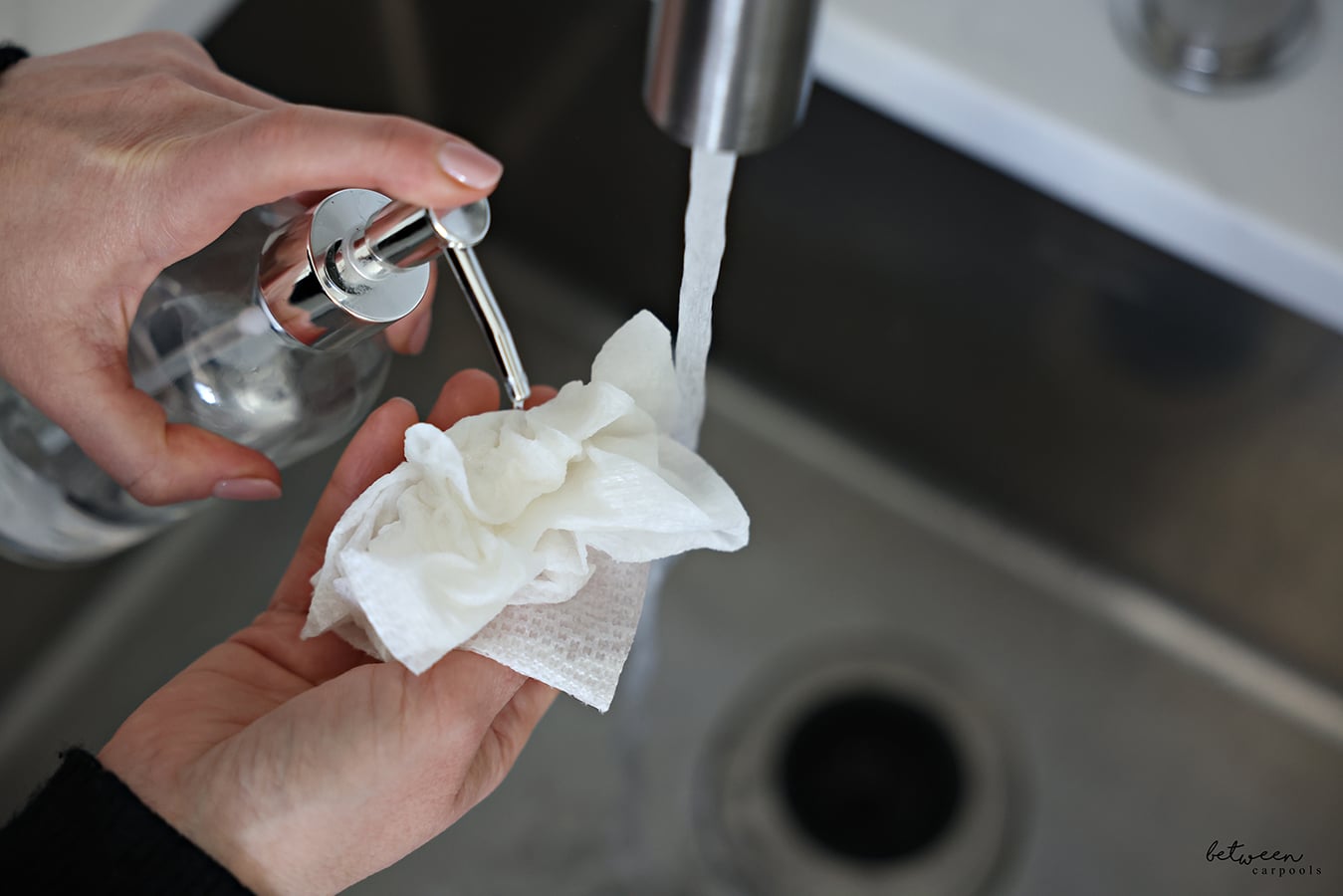 Pumping dish soap onto a wet piece of paper towel near a running kitchen sink.