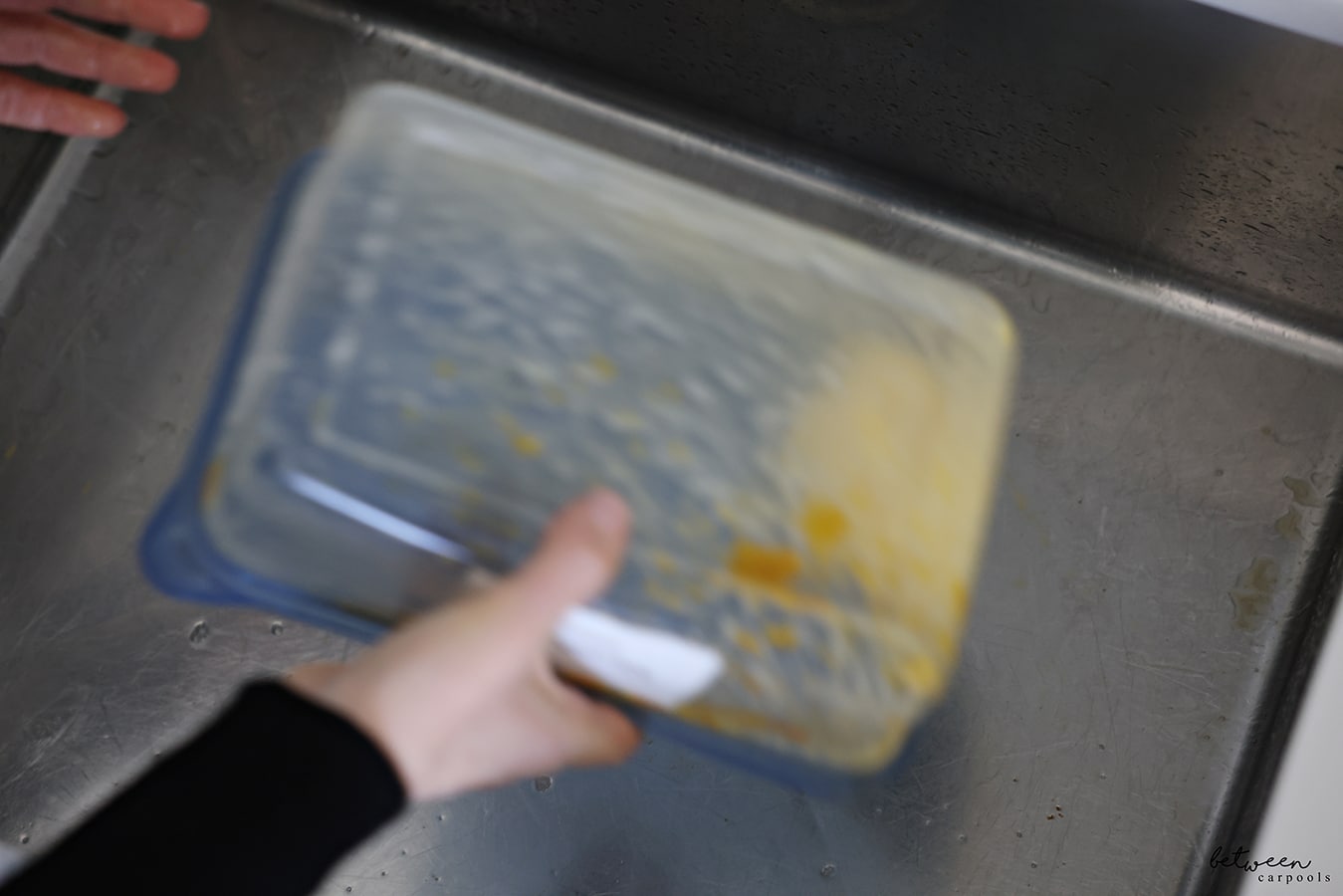 Shaking a dirty container from Meatballs with a wet piece of paper towel with dish soap inside, in a kitchen sink.