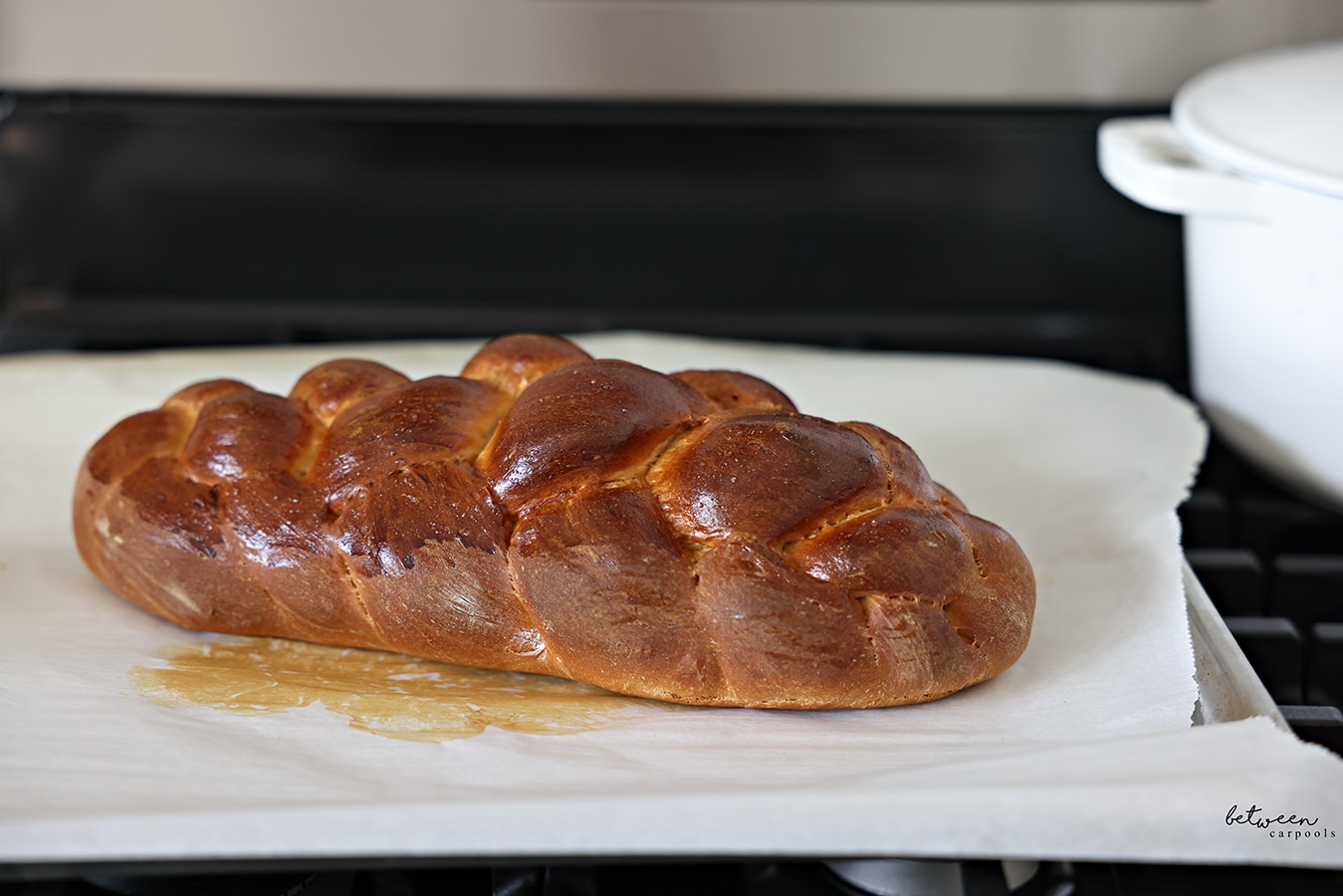 One spelt 6 strand challah, out of the oven, on a parchment lined baking sheet.