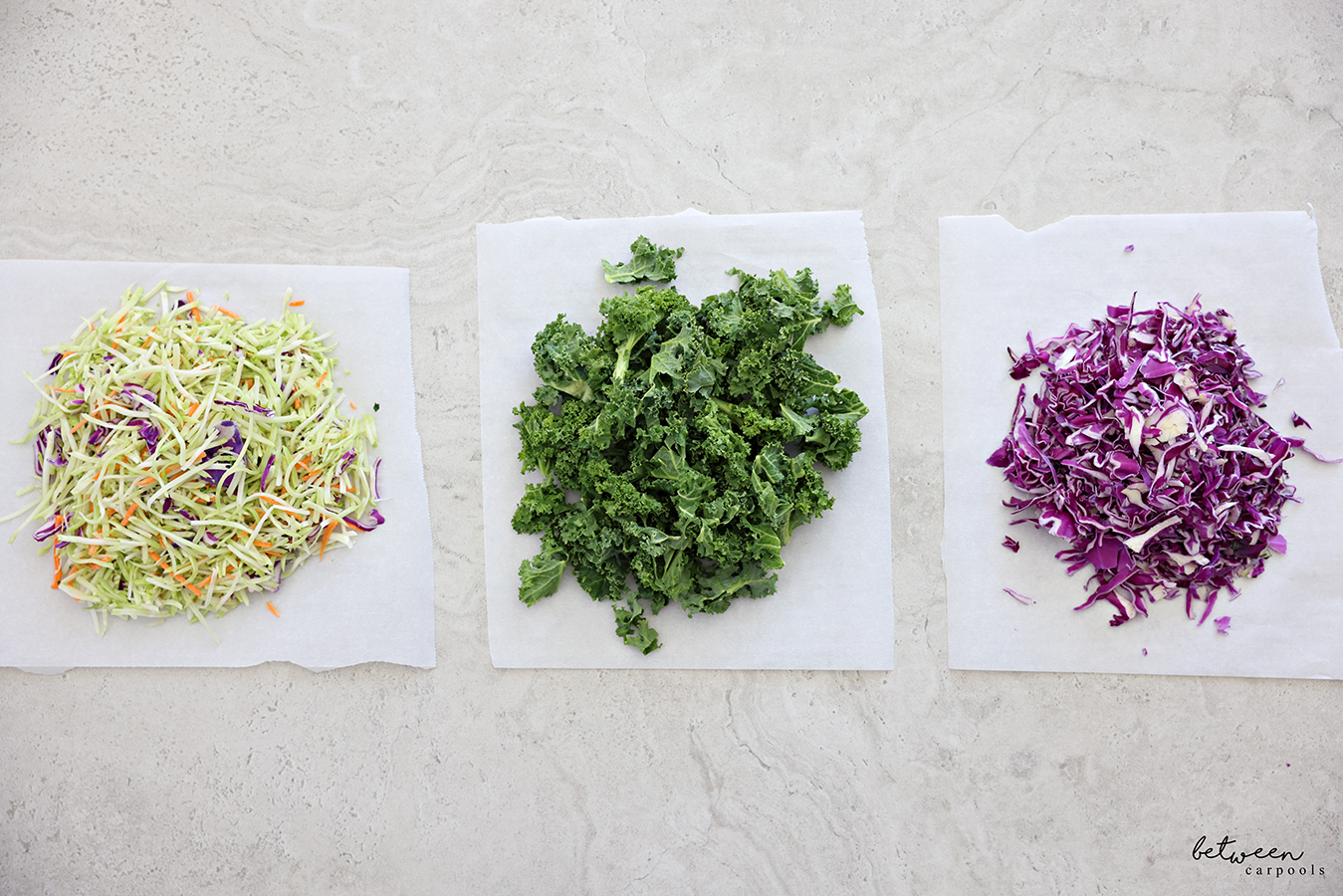 Broccoli slaw, finely chopped kale and shredded red cabbage on parchment papers.