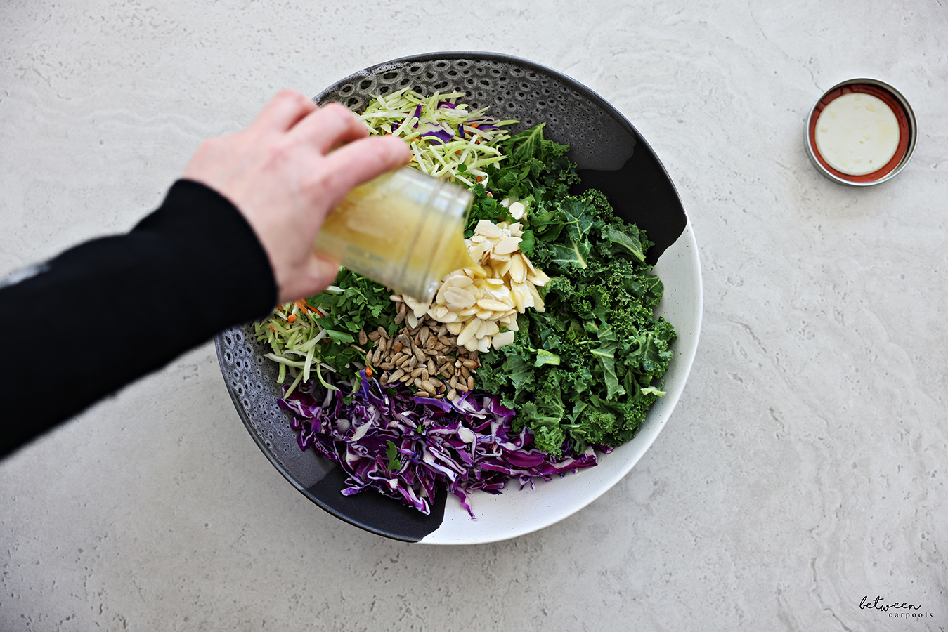Pouring lemon vinaigrette over all salad components in a large salad bowl.