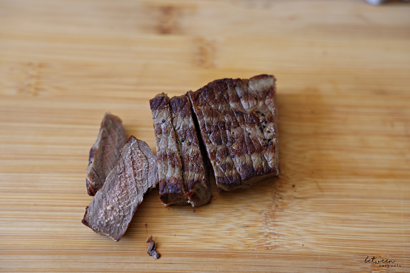 Slices of leftover grilled steak on a wooden cutting board.