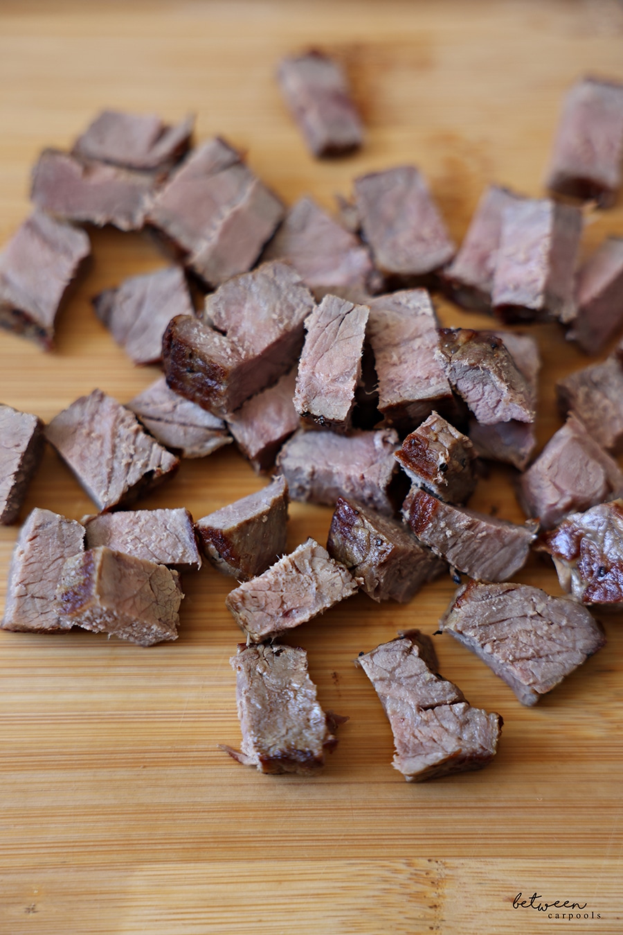 Bite-size pieces of leftover grilled steak on a wooden cutting board.