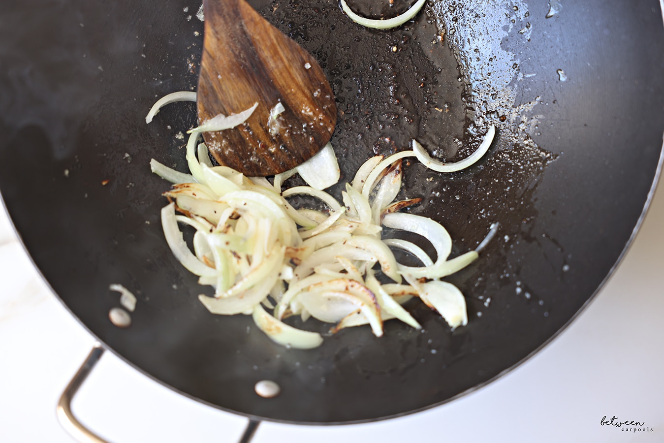 Frenched onion and minced garlic sautéing in a wok with a wooden spoon.