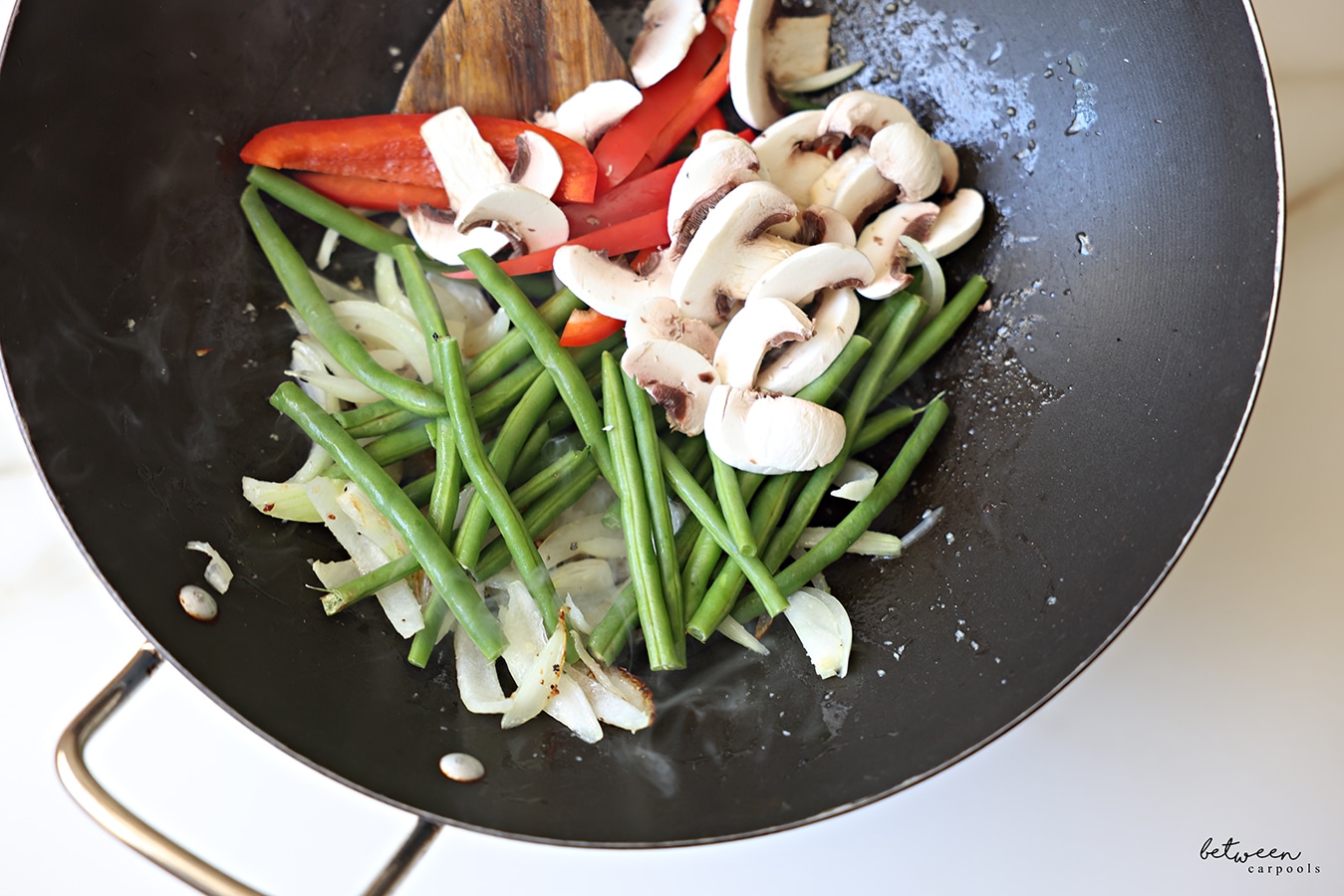 Green beans, sliced red pepper and mushrooms, added to a Frenched onion and minced garlic sautéing in a wok with a wooden spoon.