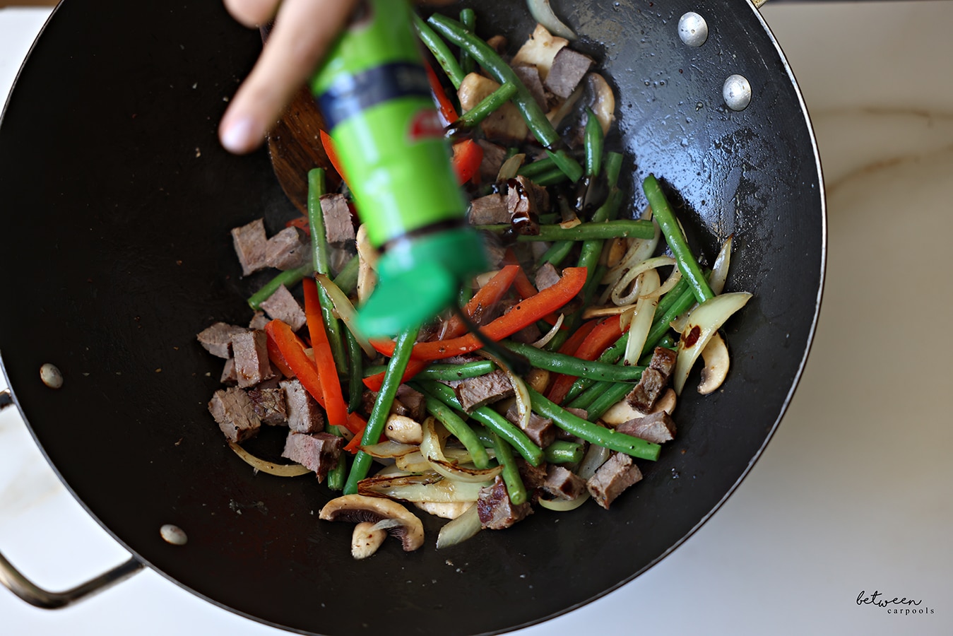 Pouring teriyaki sauce from the bottle into a wok with Leftover Steak Stir Fry.