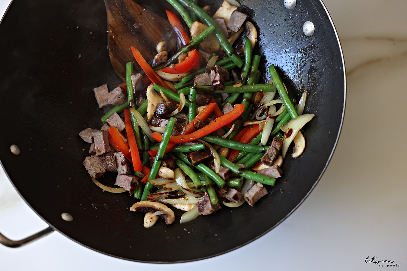 Frenced onion, minced garlic, green beans, sliced red pepper, sliced mushrooms, and leftover steak, sautéing in a wok with a wooden spoon.