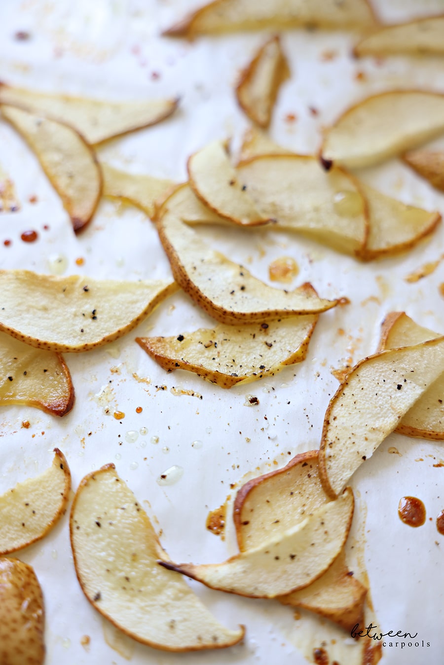 Closeup of roasted pear slices on a parchment lined baking sheet.