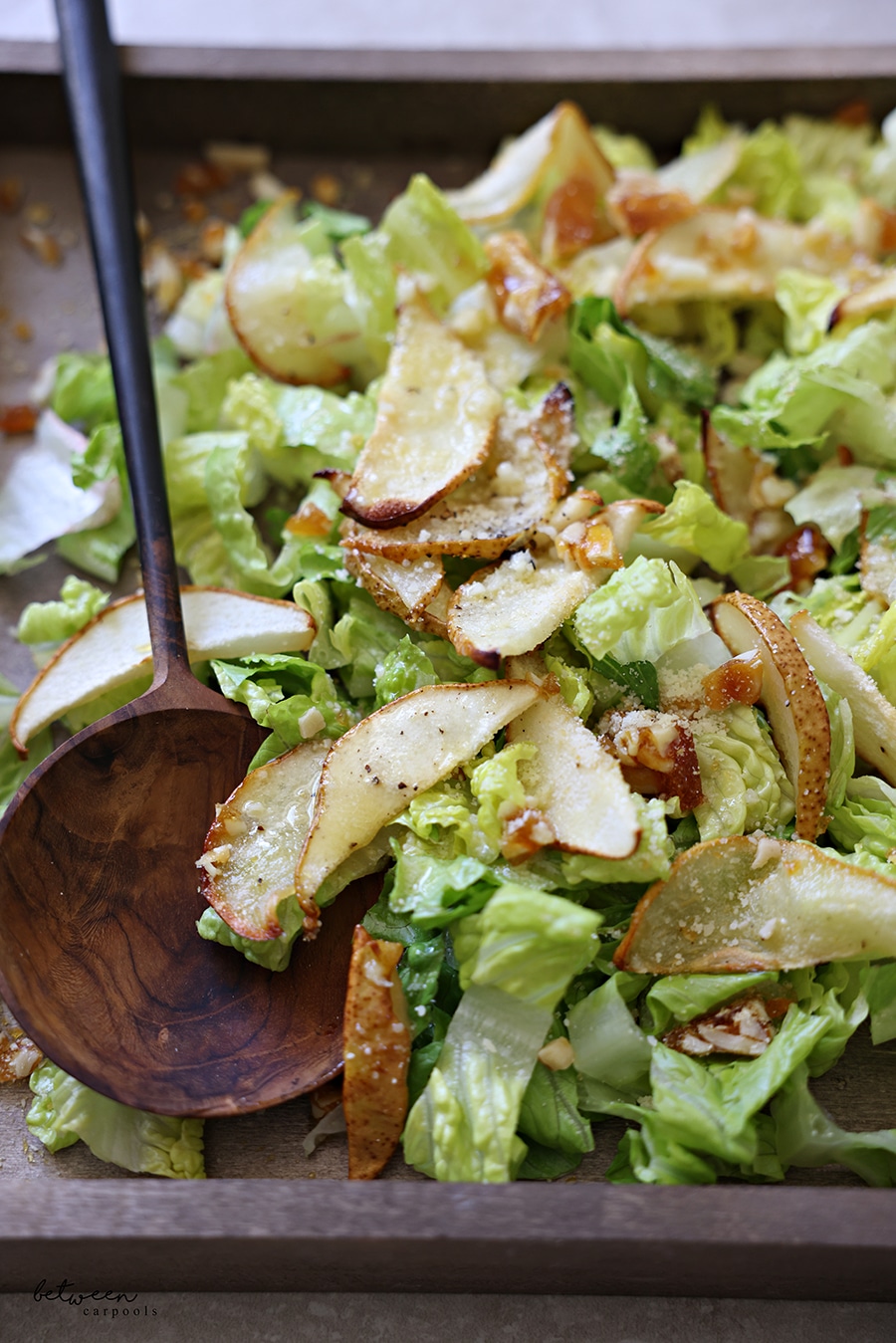 Closeup of Pear Parmesan Salad on a wooden board with serving spoon.