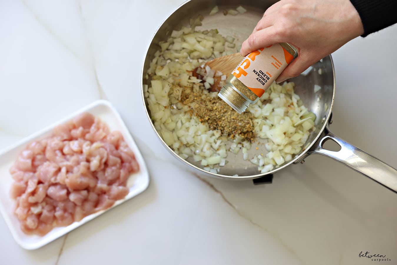 Adding Pinch Busy Chicken Blend to sautéed onion in a sauté pan. A tray of “stir fry-sized” chicken cutlets nearby.