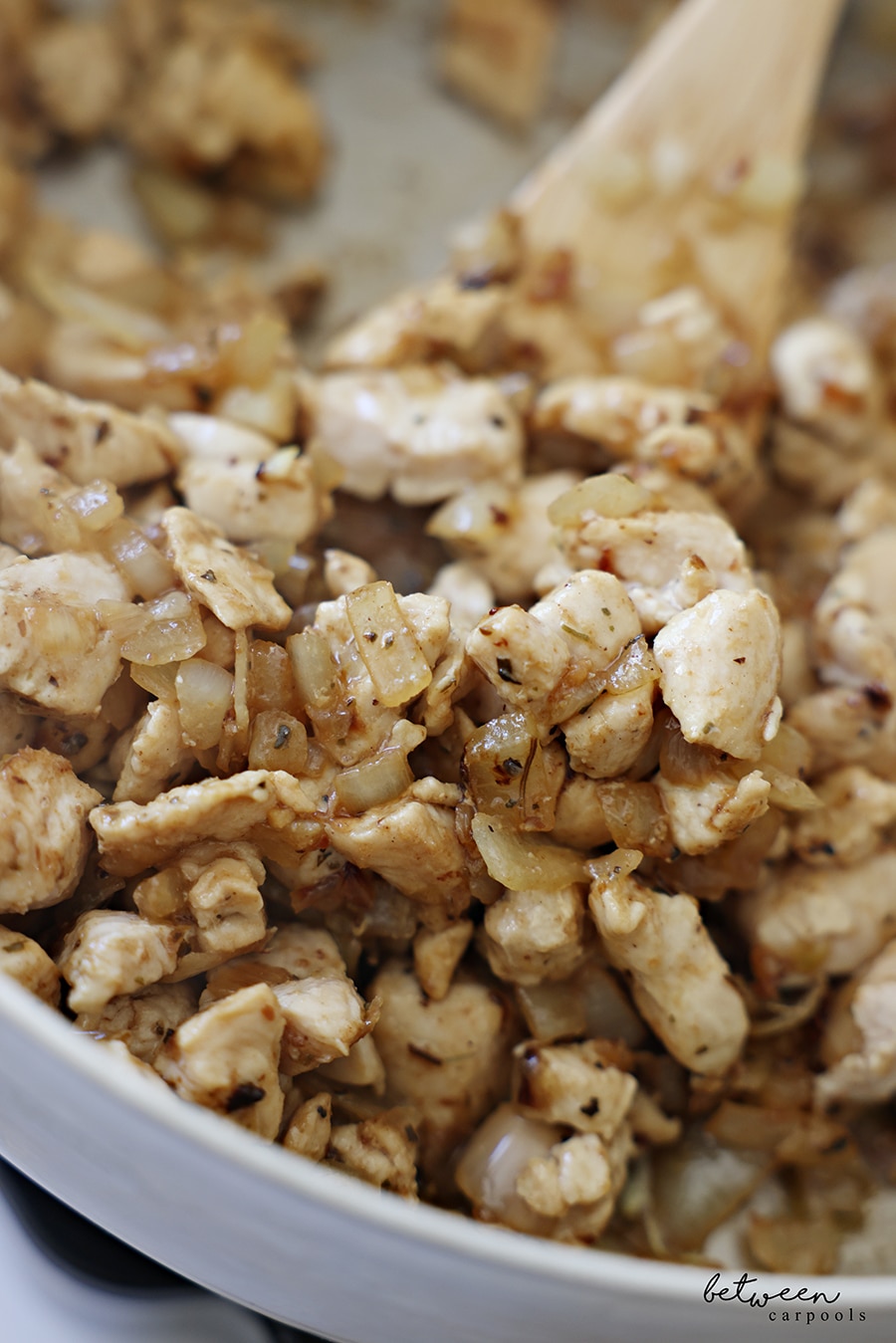 Closeup of cooked “stir fry-sized” chicken cutlets with sautéed Spanish onion and Pinch Busy Chicken Blend in a sauté pan.