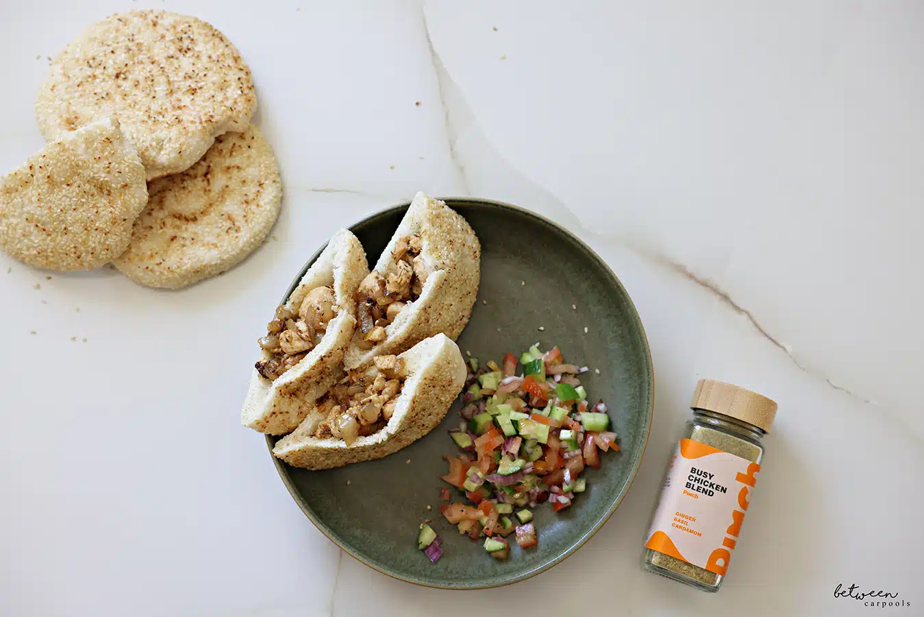 Chicken in pitas on a plate with Israeli salad. More pitas and Pinch Busy Chicken Blend nearby.