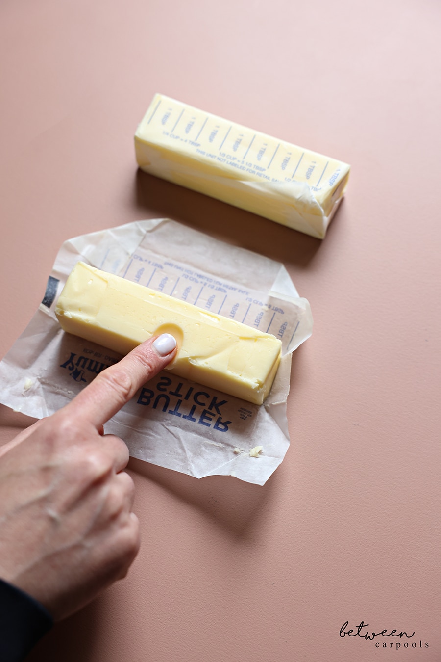2 sticks of margarine, at room temperature. Pressing an Index finger into one to show the softness. 