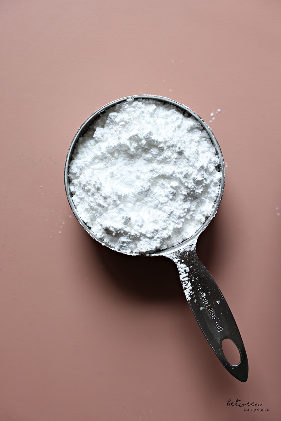 Confectioners sugar in a stainless steel 1 cup measuring cup.
