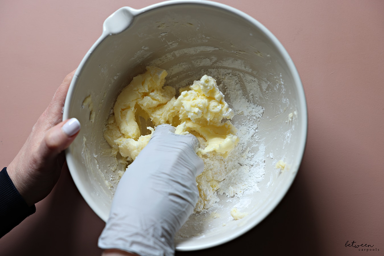 Mixing butter and confectioners sugar in a mixing bowl, with a gloved hand.