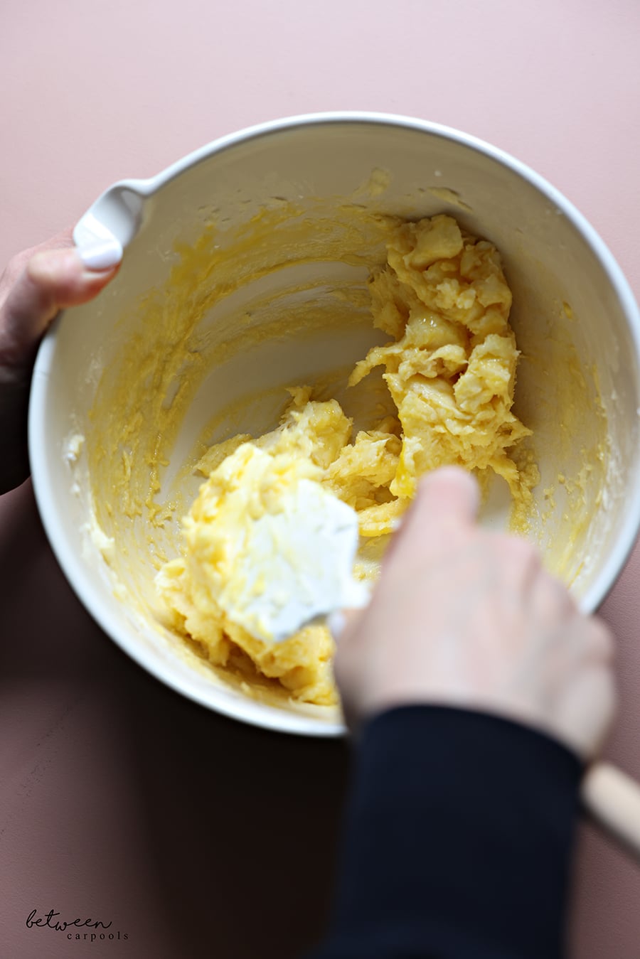 Mixing egg yolks and vanilla extract with the butter and confectioners sugar mixture, with a spatula.