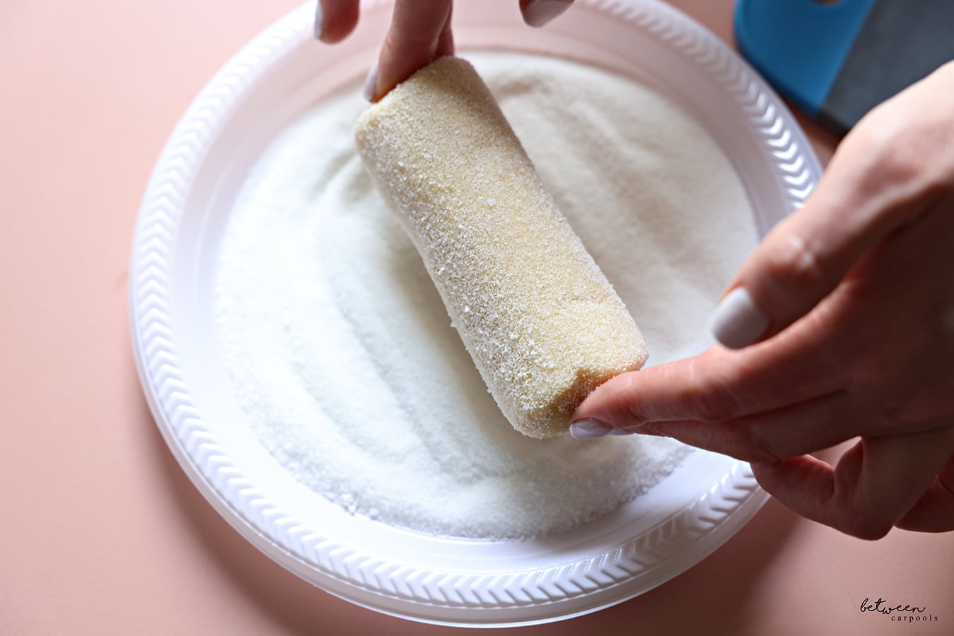 Rolling one log of French Butter Cookie dough in sugar on a plastic plate.