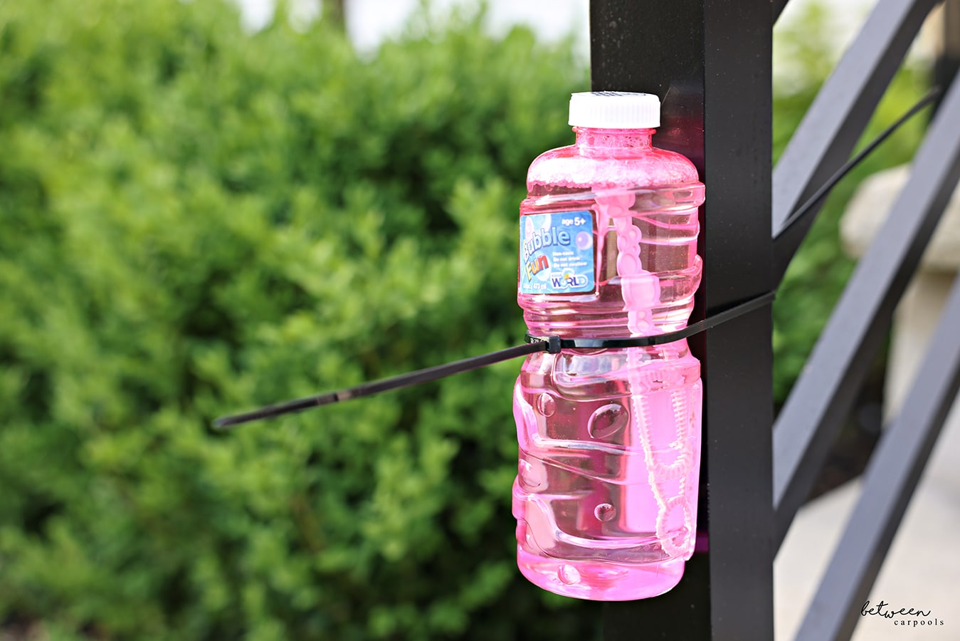 A Bubble Fun bottle zip-tied to an outdoor stairs newel post.