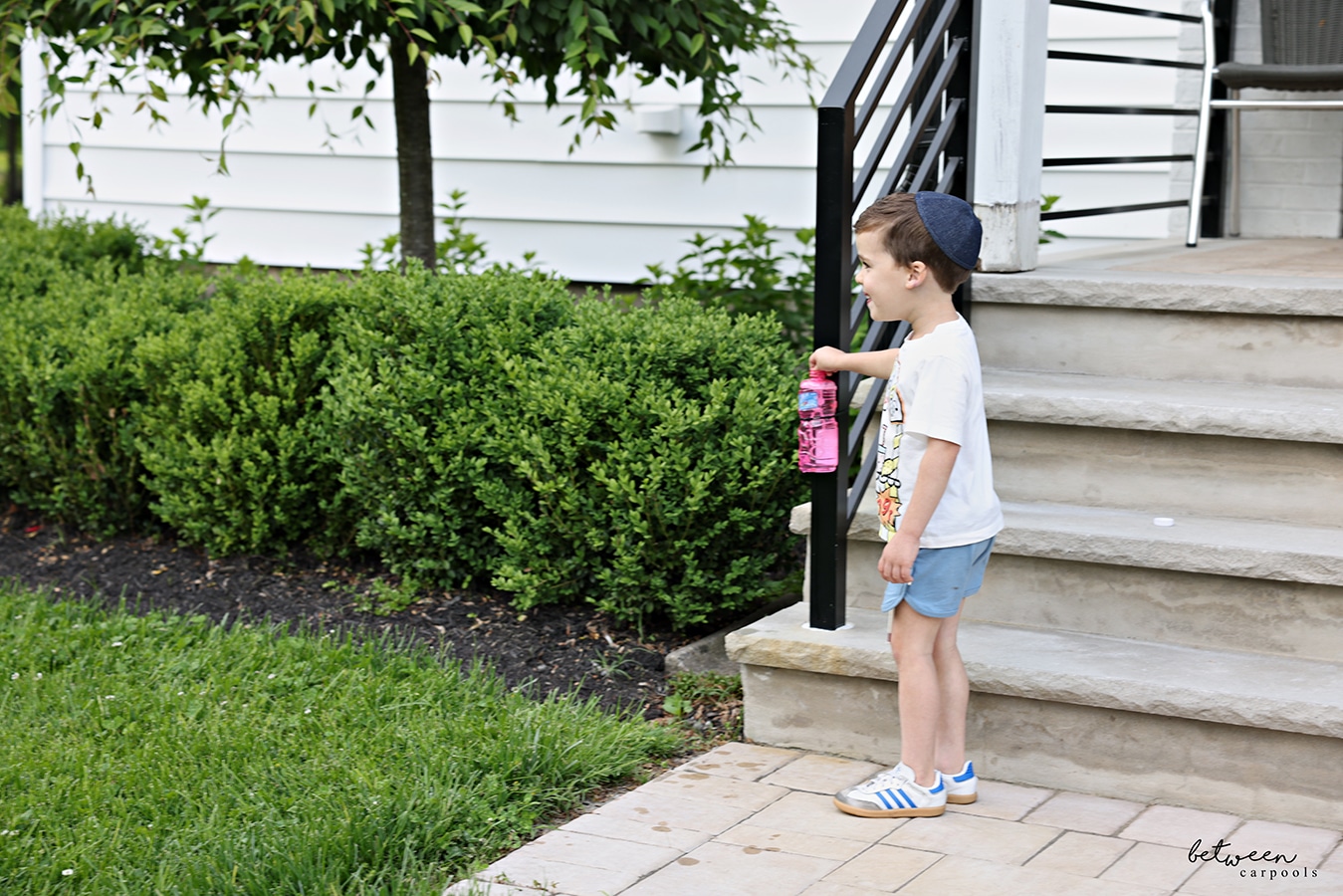A little boy dipping a bubble stick into a bottle of Bubble Fun zip-tied to an outdoor stairs newel post.