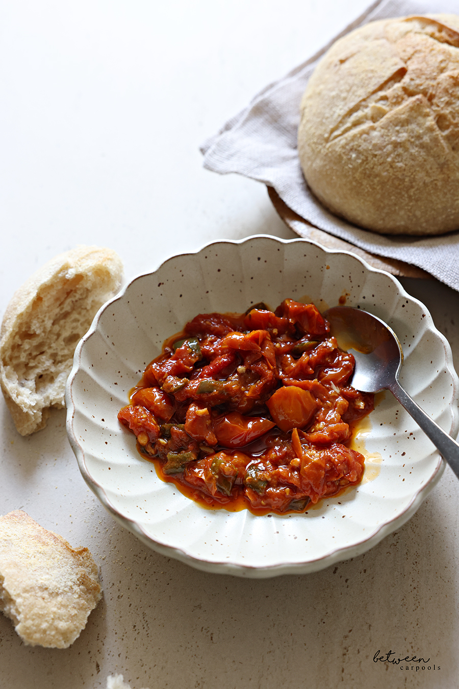 Oven matbucha in a scalloped serving bowl, sourdough nearby.
