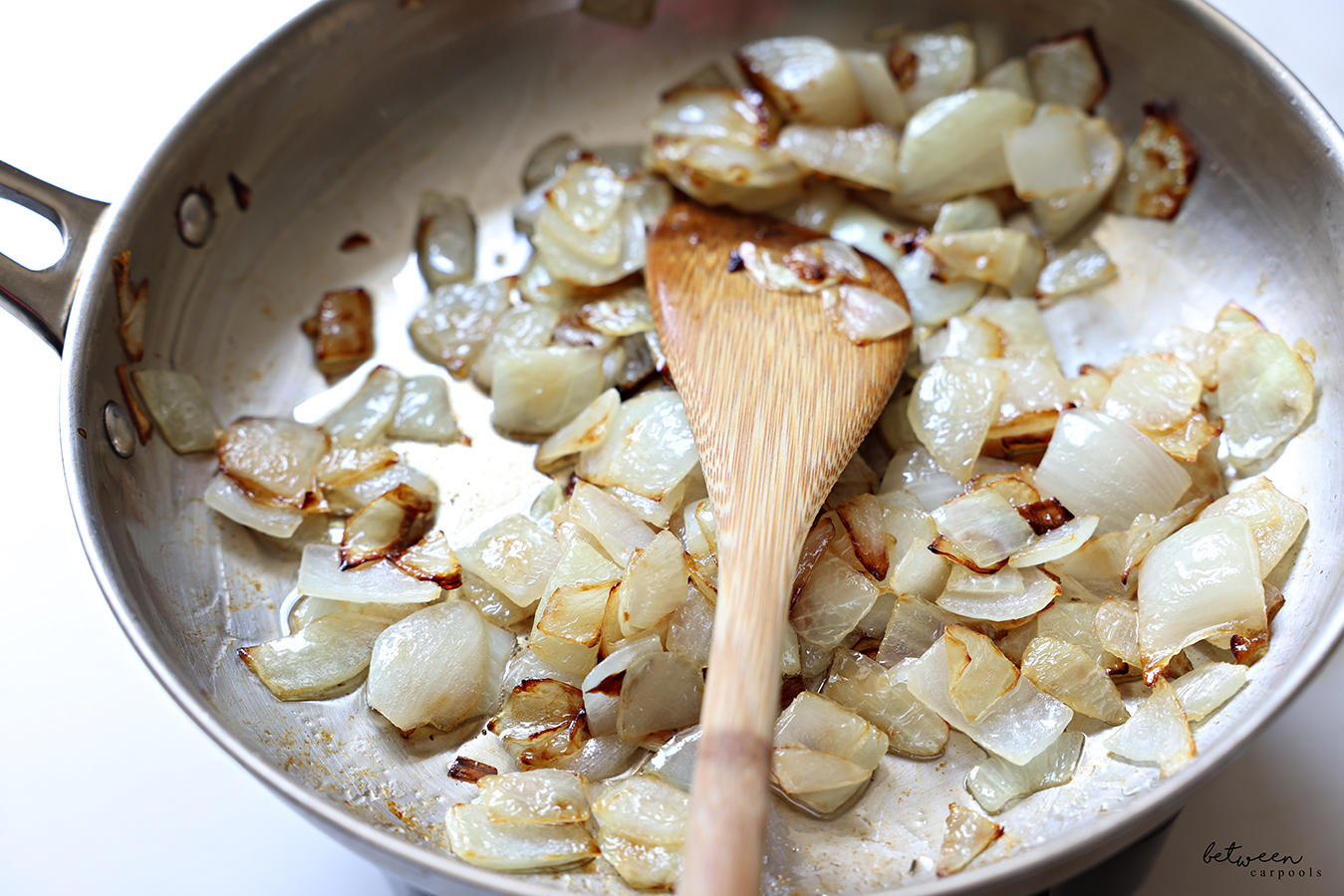 Large chunks of onion sautéing in a sauté pan with a wooden paddle.