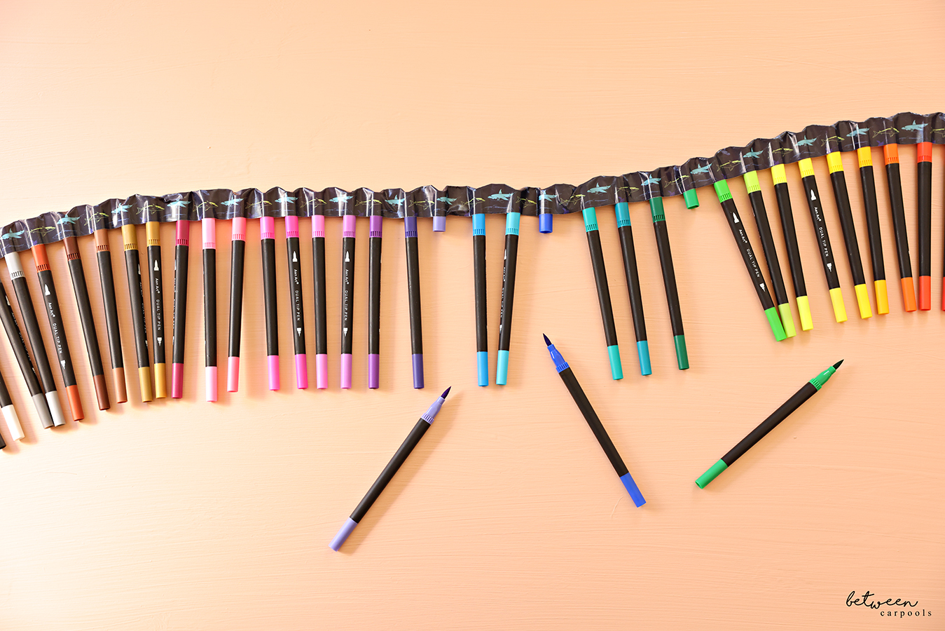 A set of markers, in shade order, its caps held together with duct tape.