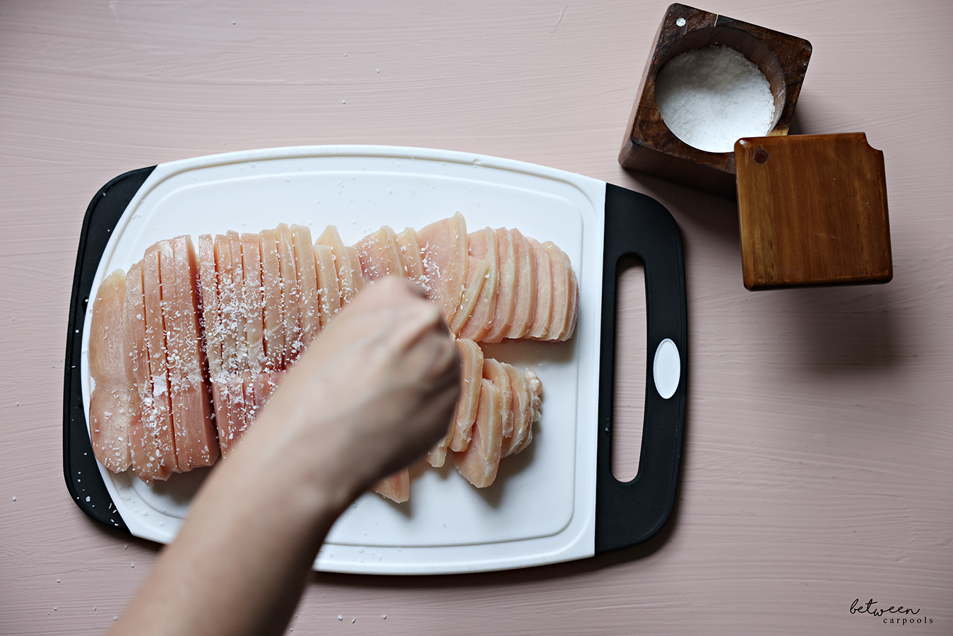 Sprinkling salt onto slices of frozen chicken on a cutting board.