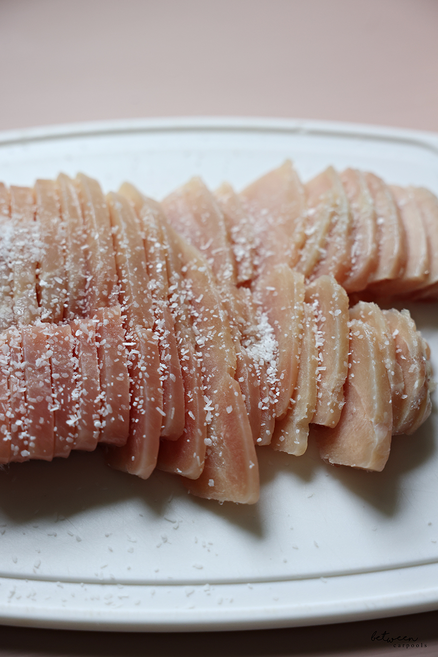 Closeup of slices of frozen chicken, sprinkled with salt, on a cutting board.