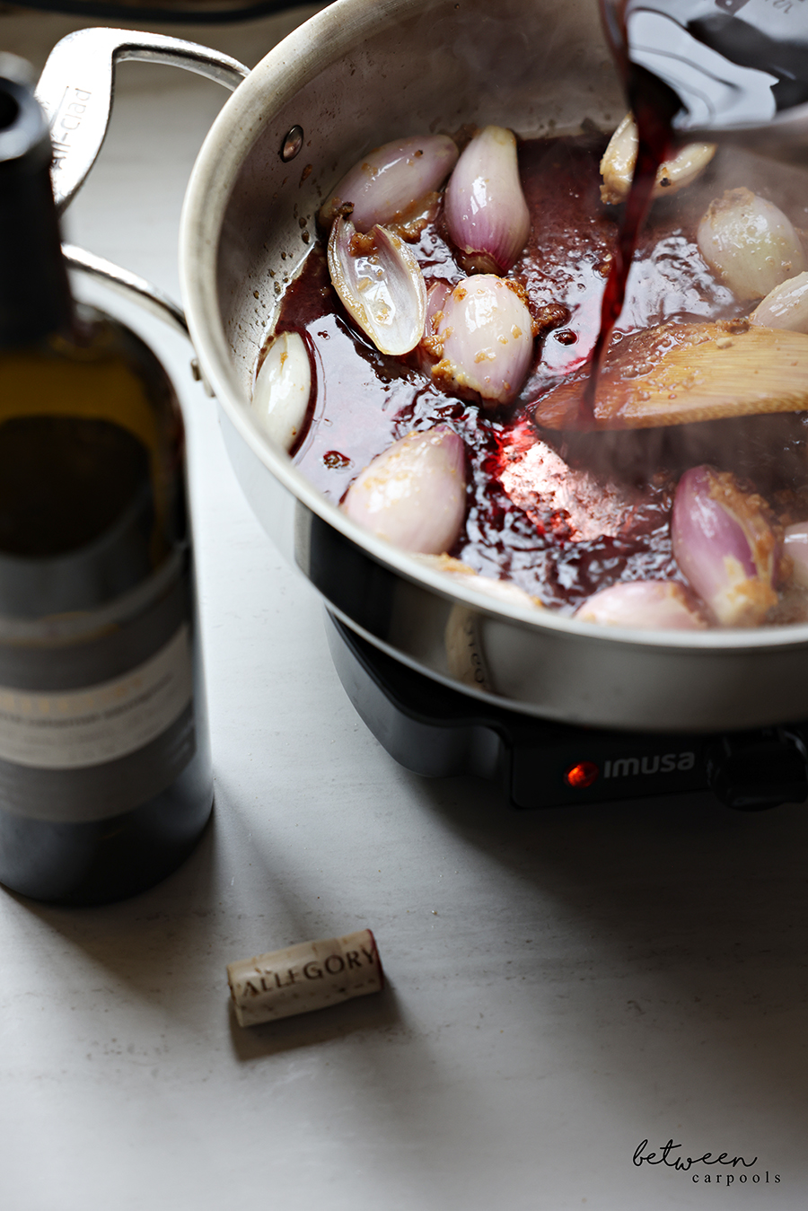 Adding red wine to sautéed halved shallots, garlic, thyme, and rosemary.