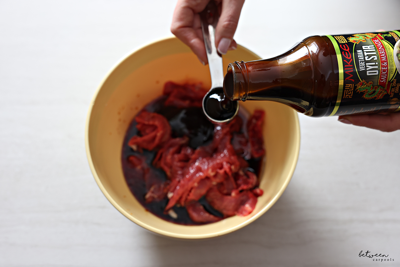 Measuring Mikee Oyster Sauce over a bowl with thinly sliced steak and marinade.
