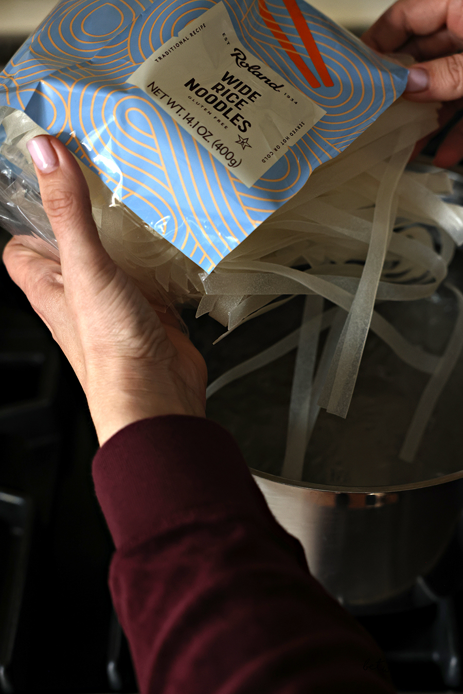 Holding a bag of Roland Wide Rice Noodles.