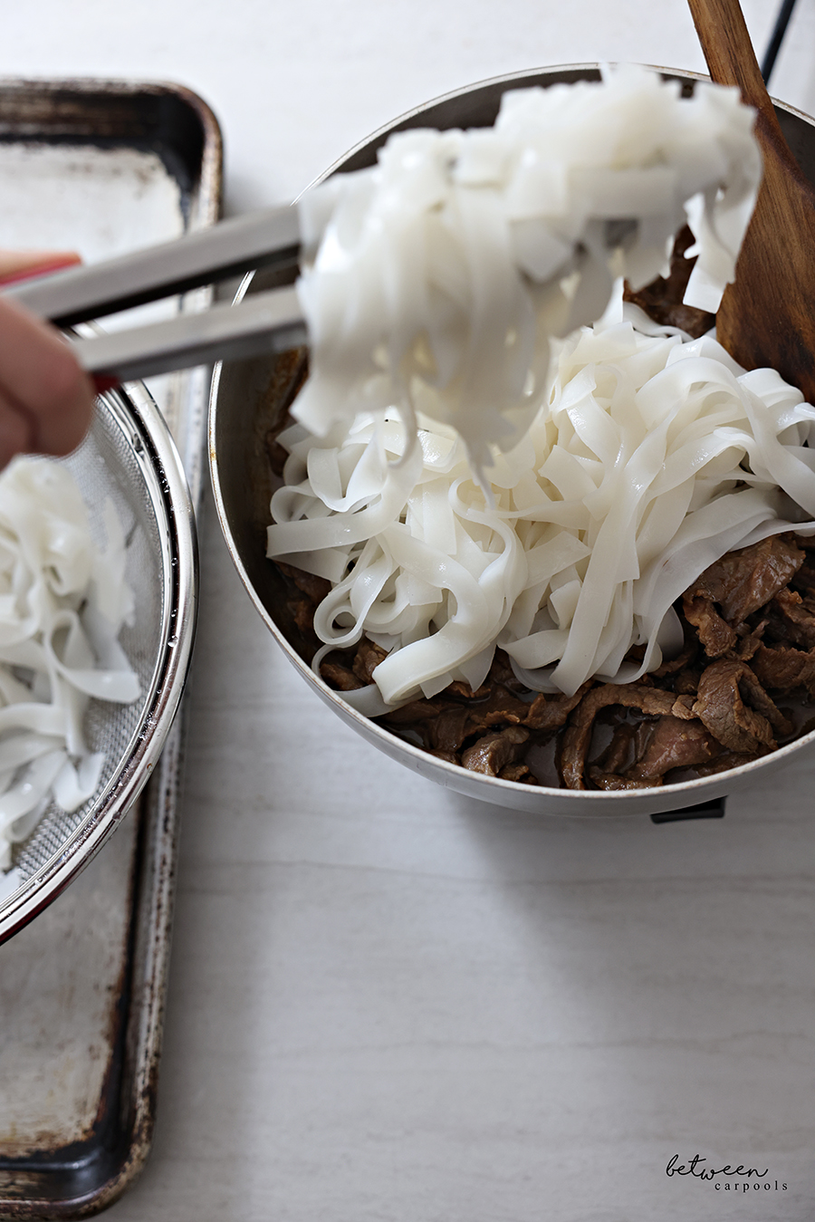 Adding cooked Wide Rice Noodles to a large pan with stir-fried steak.